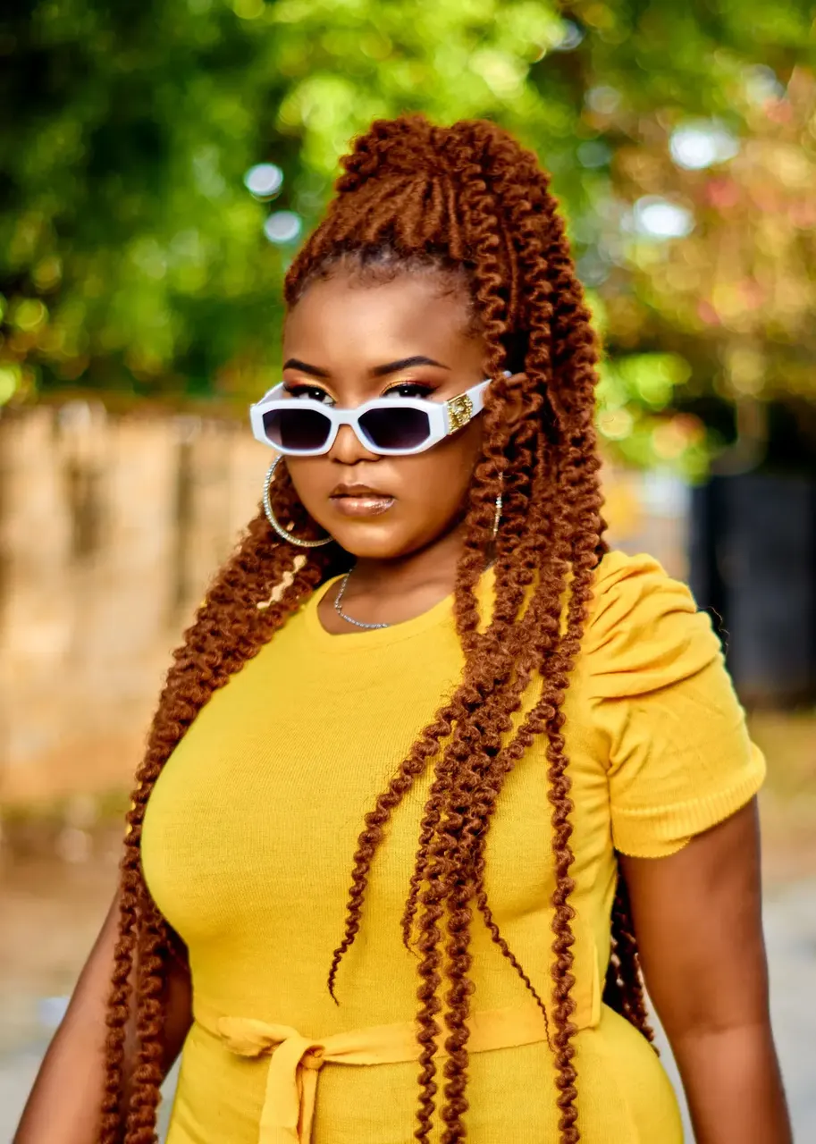 Outdoor portrait of a woman with braids, sunglasses and a yellow outfit